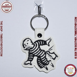 White Key Chain with black stitching of a man getting kicked in the rear end.