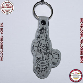 Grey key chain with black stitching in the shape of a ship