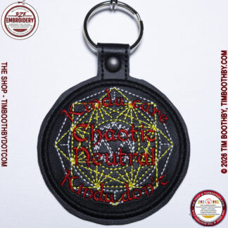 Round black key chain with yellow dice shaped stitching and red words saying chaotic neutral